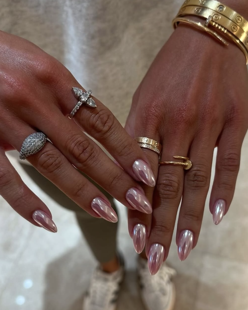 A side-by-side editorial view of long, almond-shaped nails with a high-shine pink chrome finish and a metallic iridescent glow.