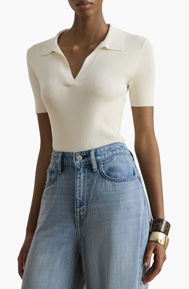 A close-up of a person wearing light-wash high-waisted wide-leg denim jeans with a silver button closure, paired with a white ribbed short-sleeve top.