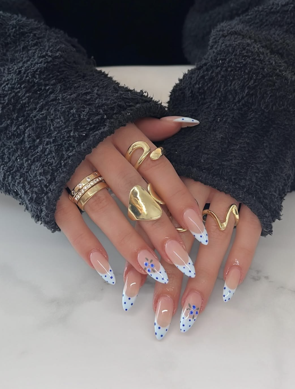 A high-feminine spring manicure by @amanda_nailingit featuring almond-shaped nails with a white base, intricate blue floral designs, and regal gold foil accents.