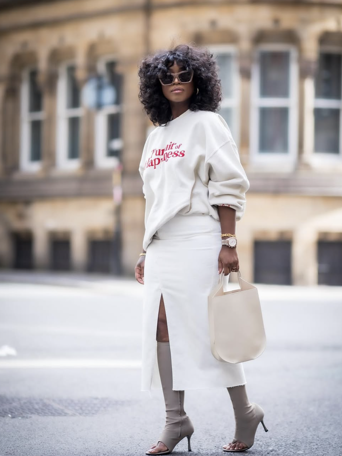 Woman wearing a white slit midi skirt with a graphic sweatshirt and beige sock boots