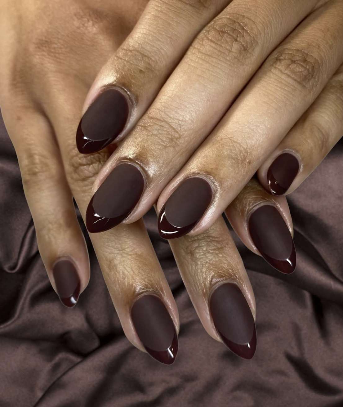 A close-up of natural nails featuring a velvety matte cocoa brown manicure with a gold ring accent.