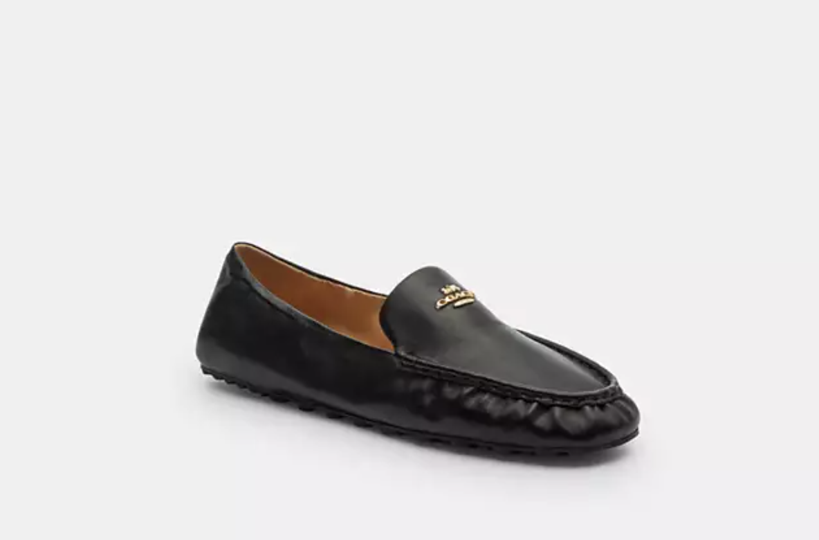 A pair of Coach Phoebe soft leather loafers in black with a classic almond toe and gold-tone logo hardware on the vamp.
