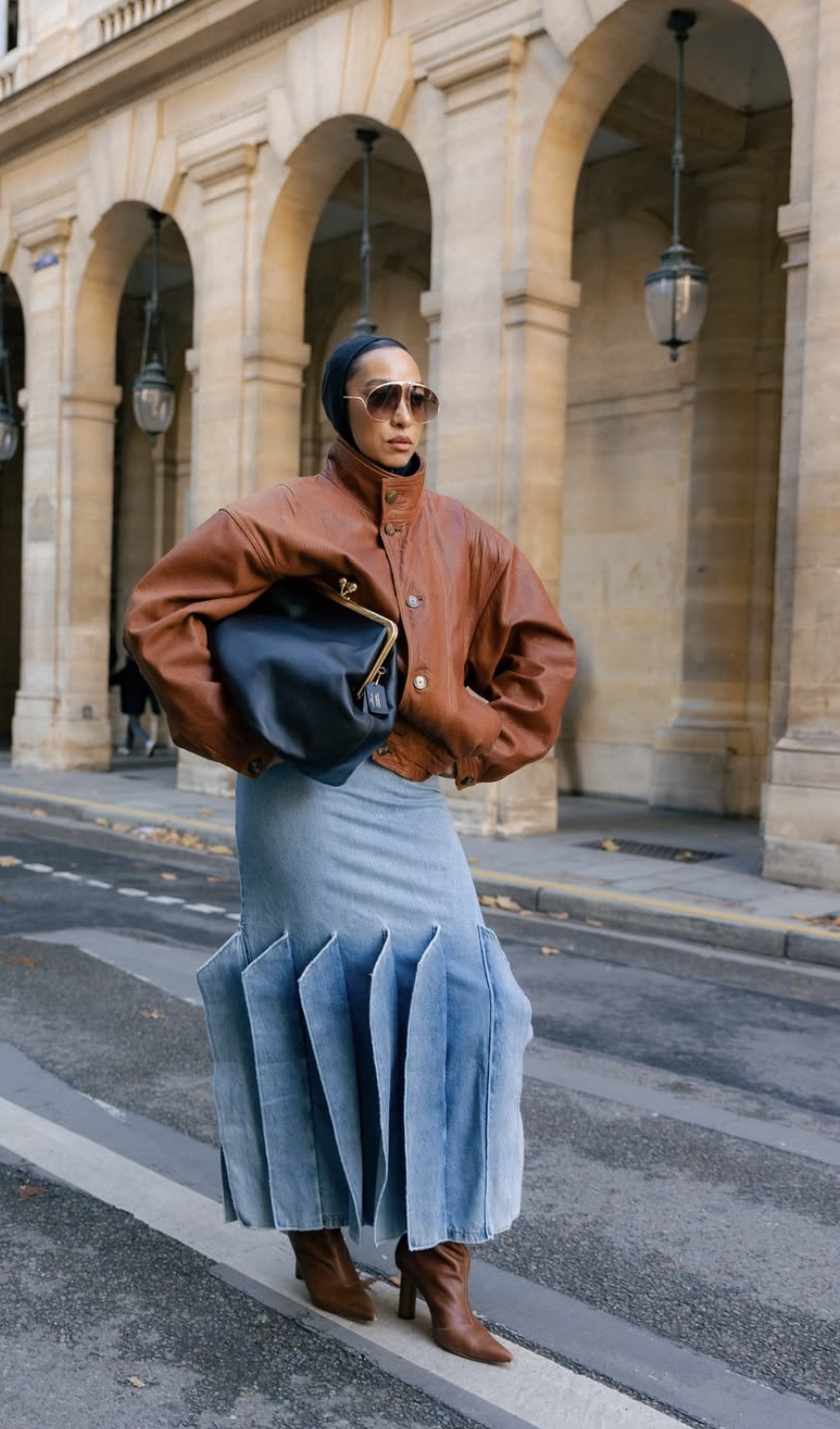 Woman wearing a pleated denim midi skirt with a cognac leather bomber jacket and cognac boots