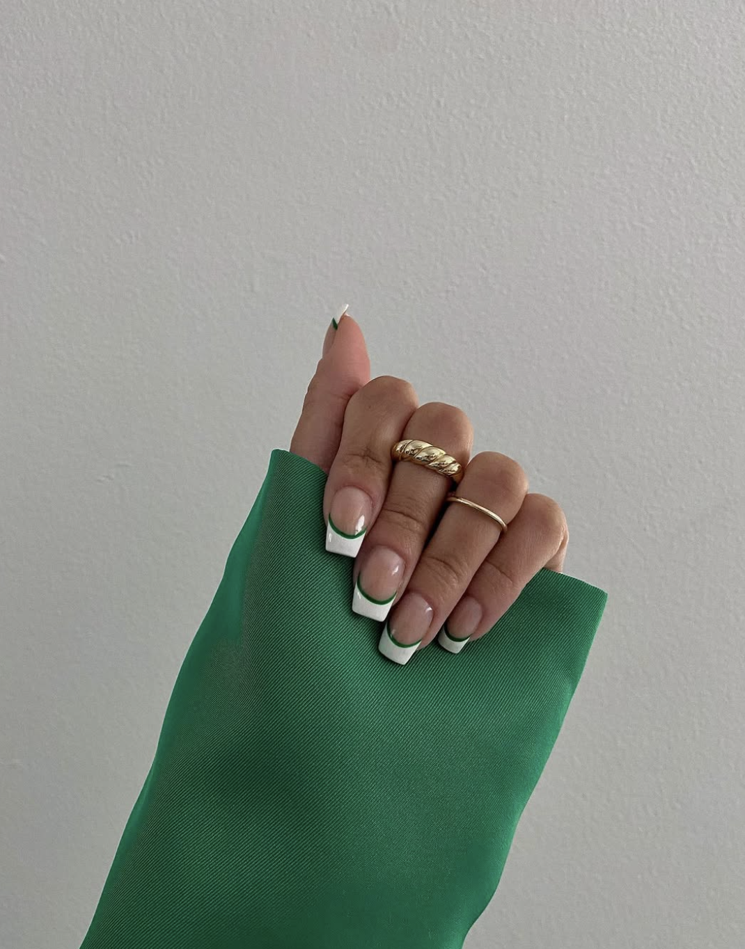 Long square-shaped nails with a double French tip design in crisp white and vibrant green, styled with a gold croissant ring.