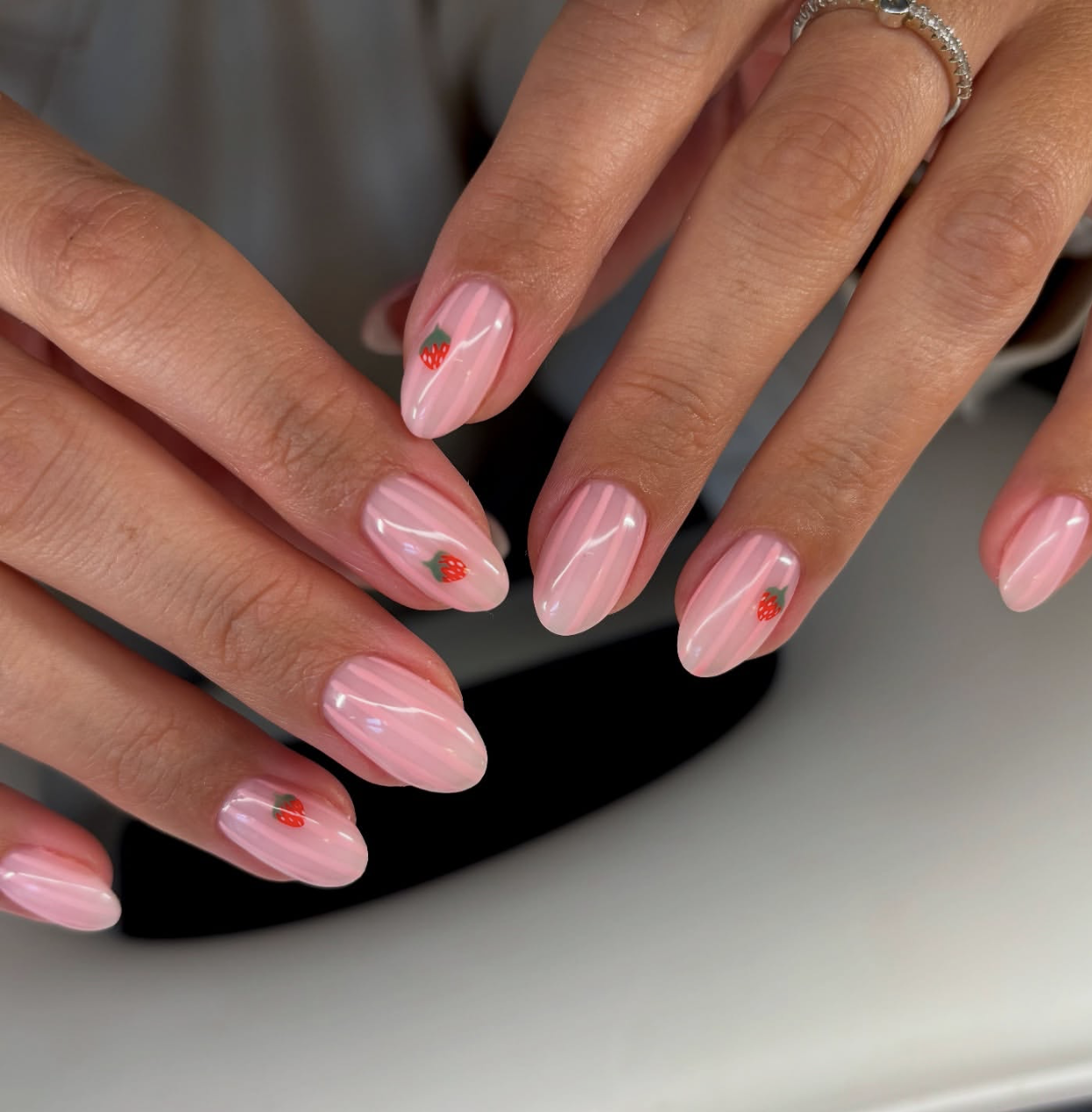 Long almond shaped nails with a light pink base, white vertical stripes, and tiny hand-painted strawberry accents.