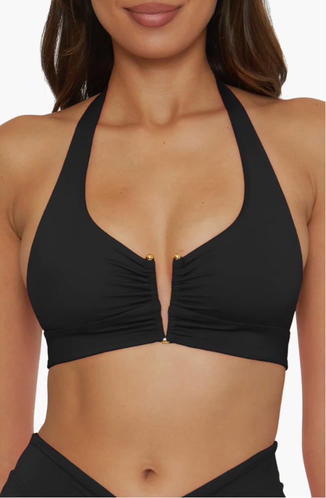 A woman wearing a black halter bikini top with a deep V-wire neckline, shirred fabric detailing, and gold bead accents on the straps.