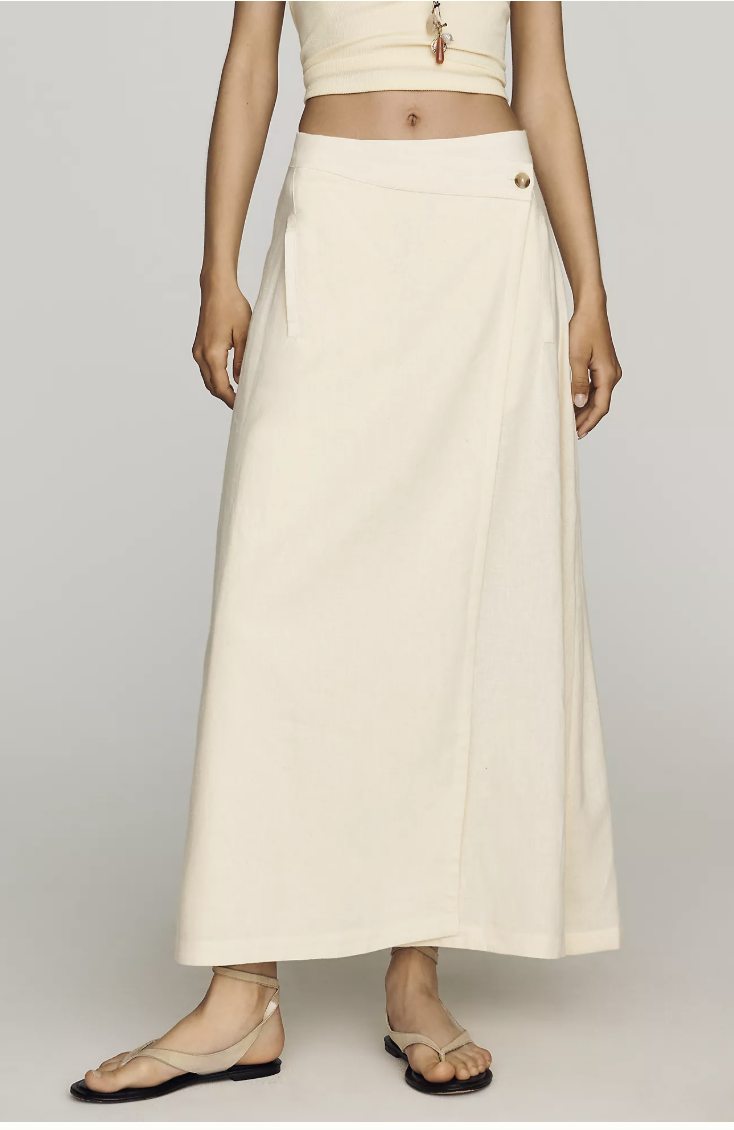 Close-up of beige flat ankle-strap sandals styled with a cream linen maxi skirt.