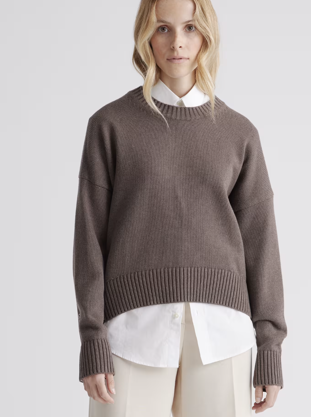 Taupe-brown crewneck knit sweater layered over a white collared shirt.