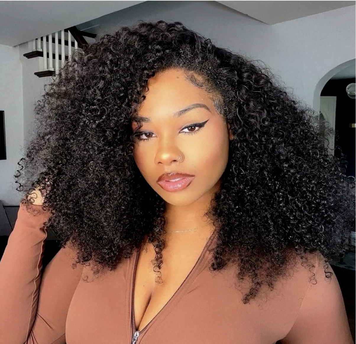 Woman wearing a voluminous 24-inch curly human-hair half wig with a fitted brown top.
