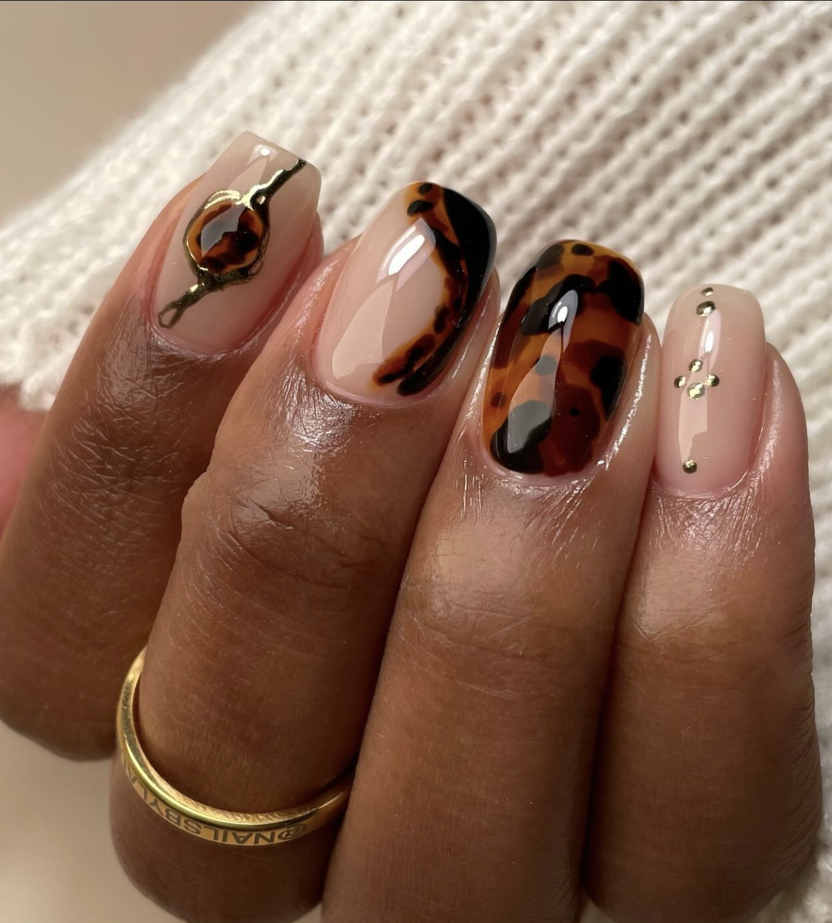 Close-up of short nails featuring a glossy caramel brown manicure with subtle torties accents and gold rings.