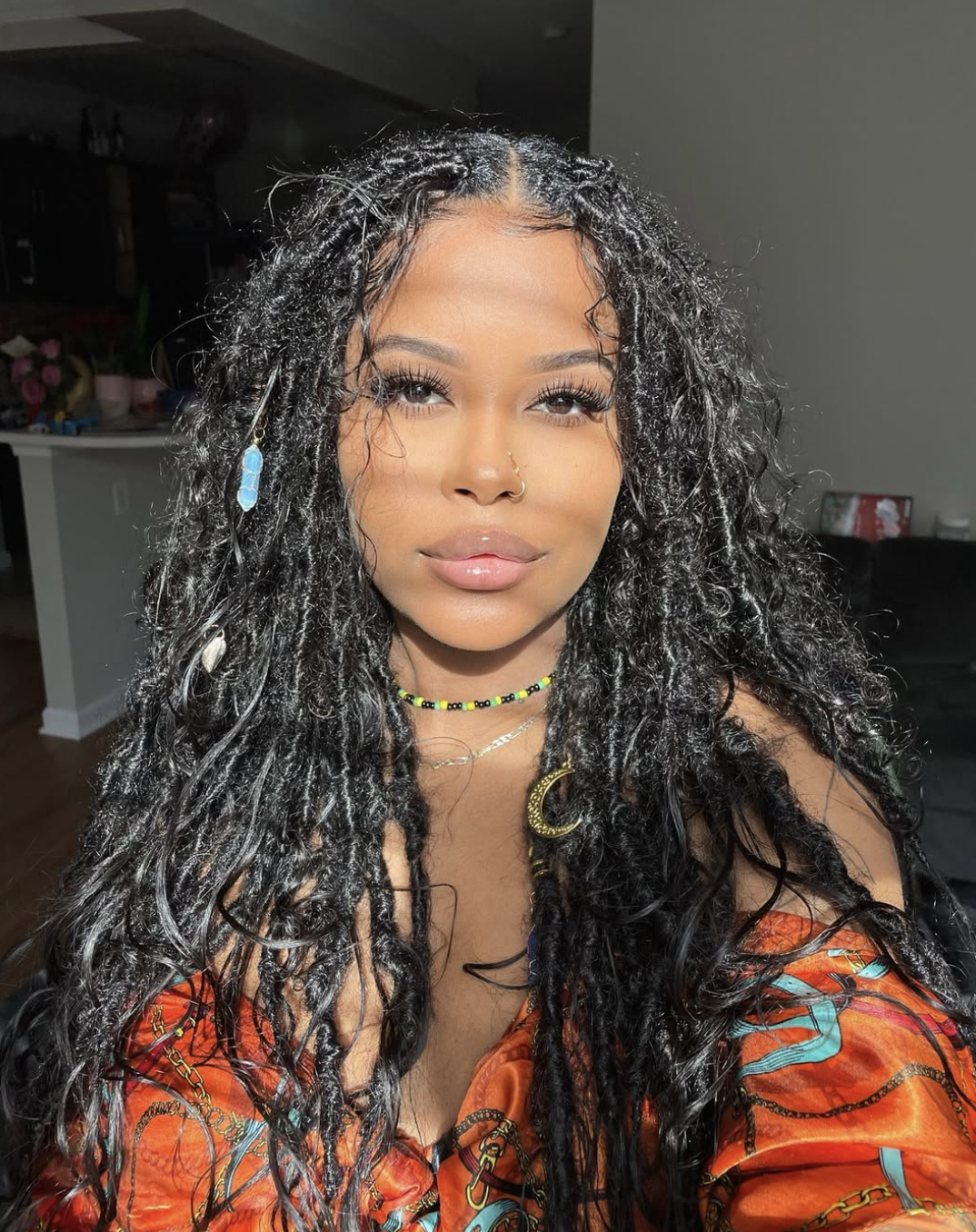 A woman with an oval face shape wearing long, voluminous boho goddess locs with curly tendrils and face-framing layers.