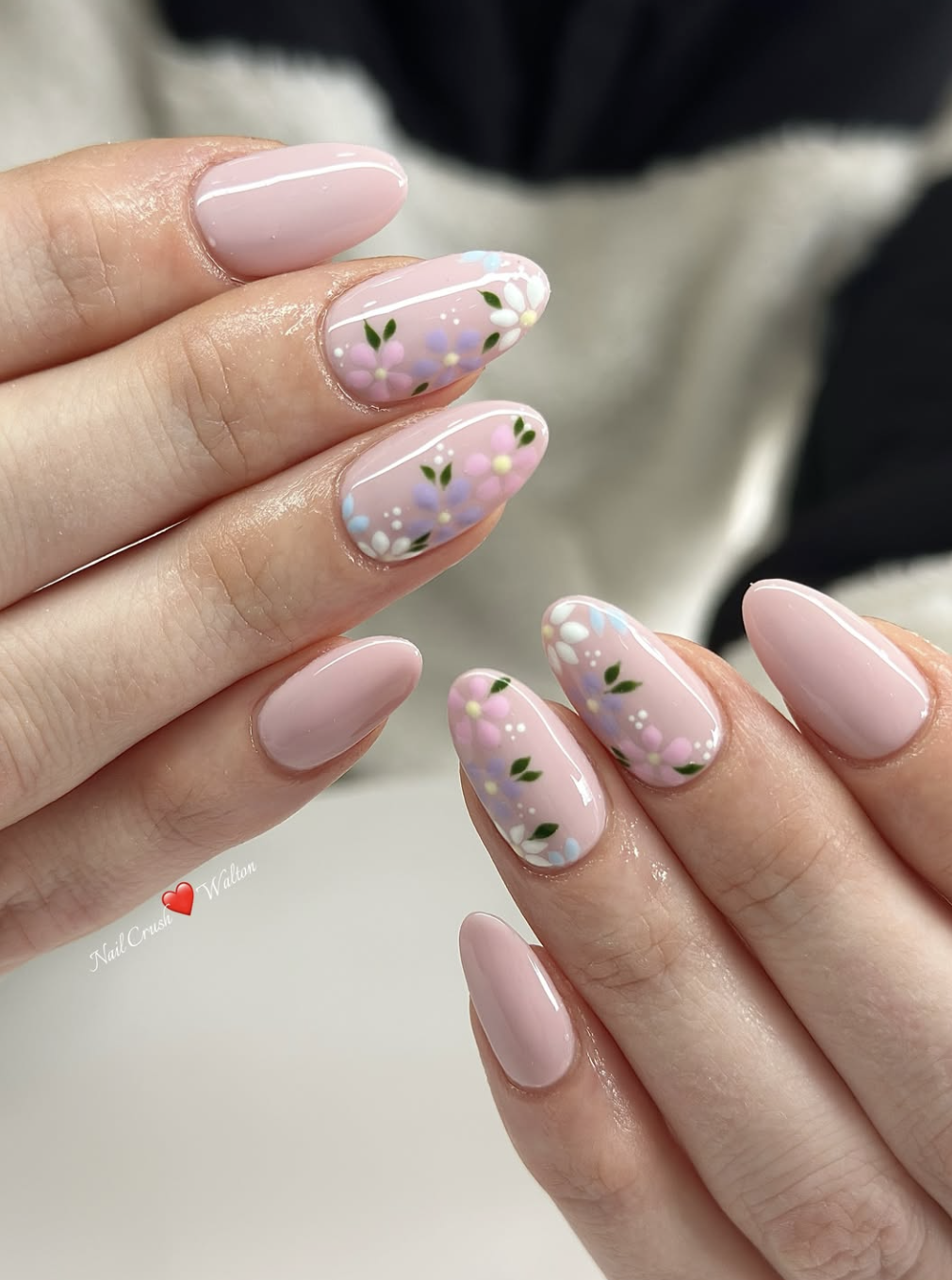 Oval-shaped pink nails with accent nails featuring detailed purple and white hand-painted flowers.