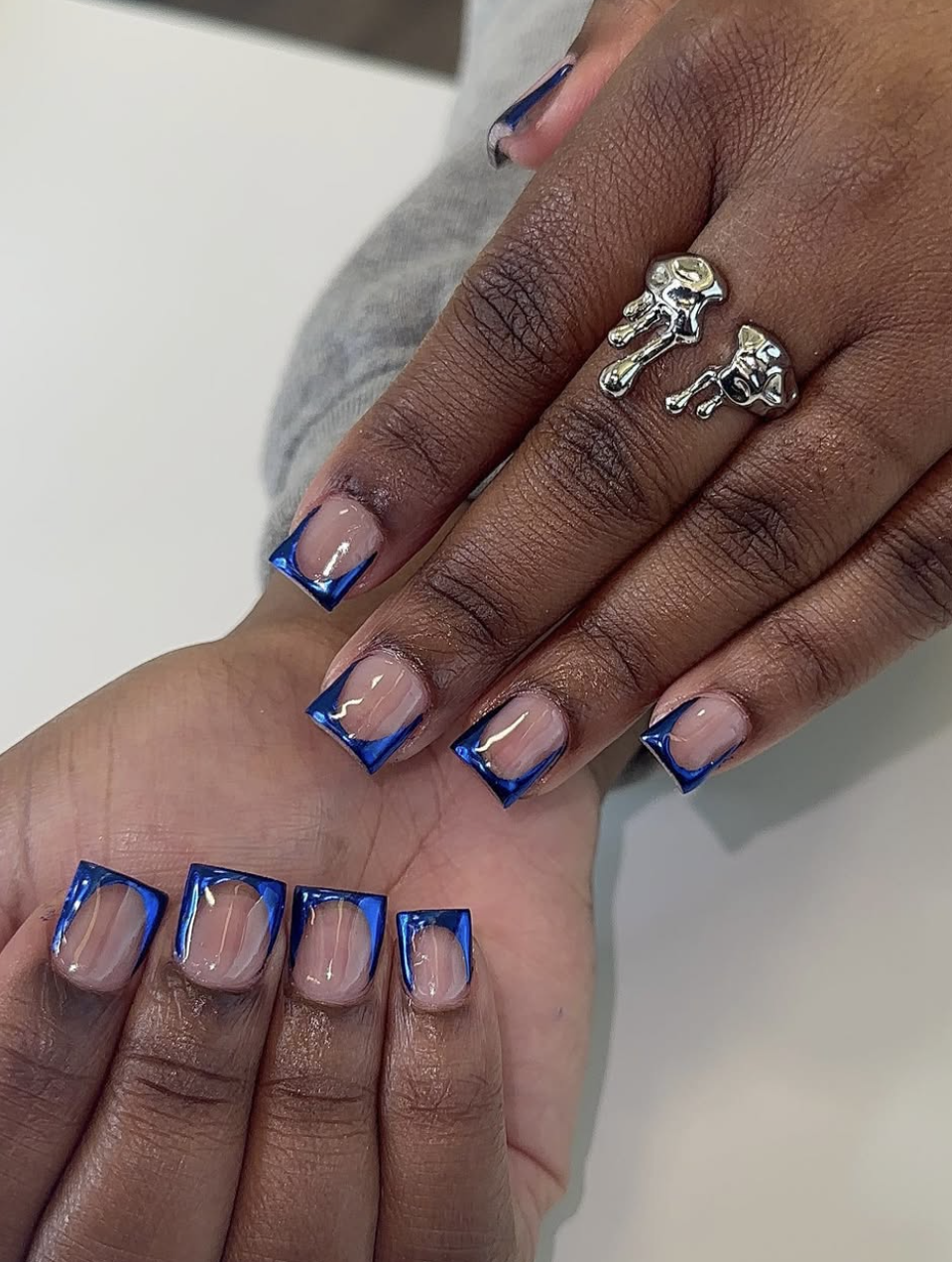 A close-up of short nails featuring a vivid cobalt blue French tip outline design over a natural nude base.