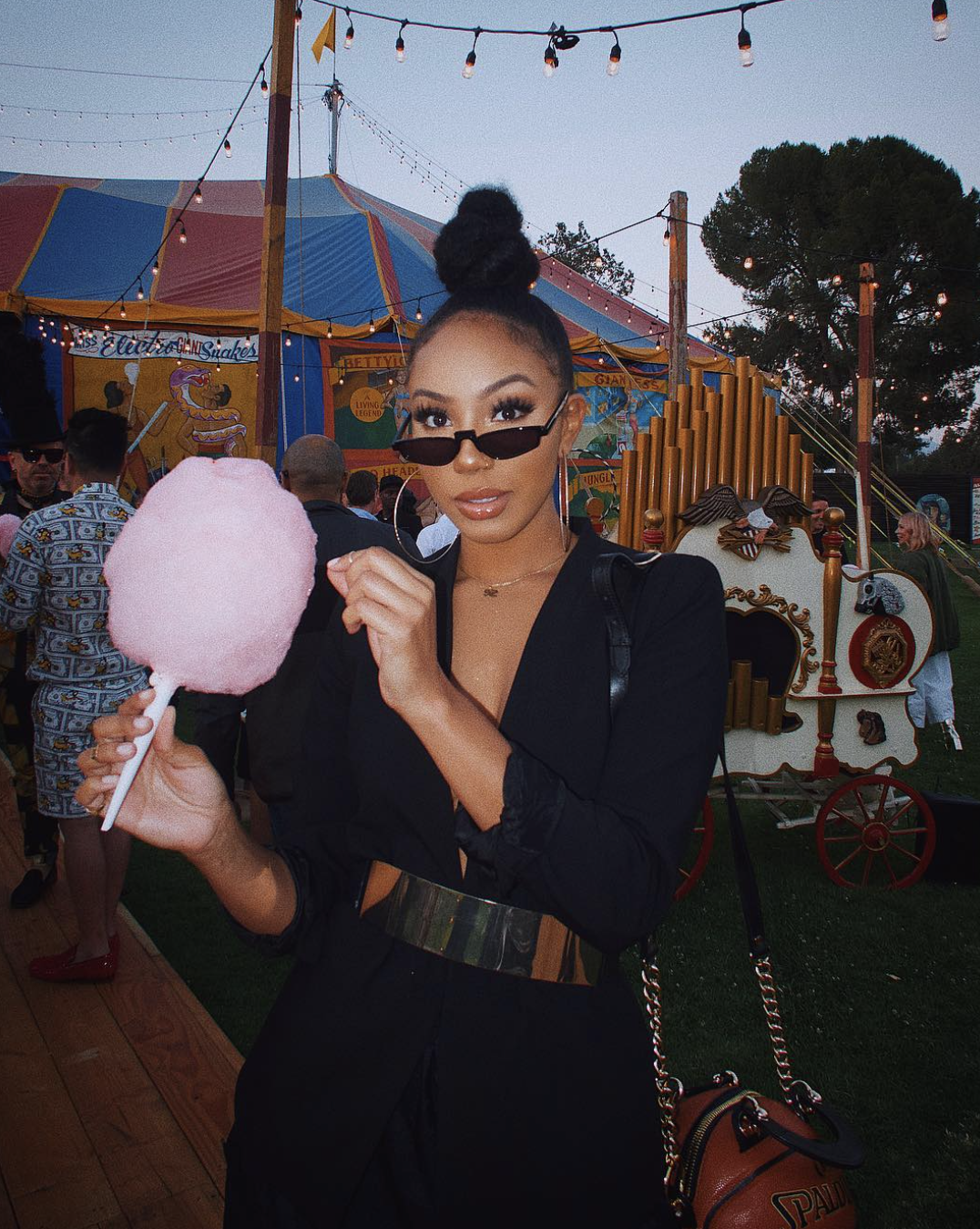 A woman with an oval face shape wearing a high curly puff with sleek laid edges, holding pink cotton candy.