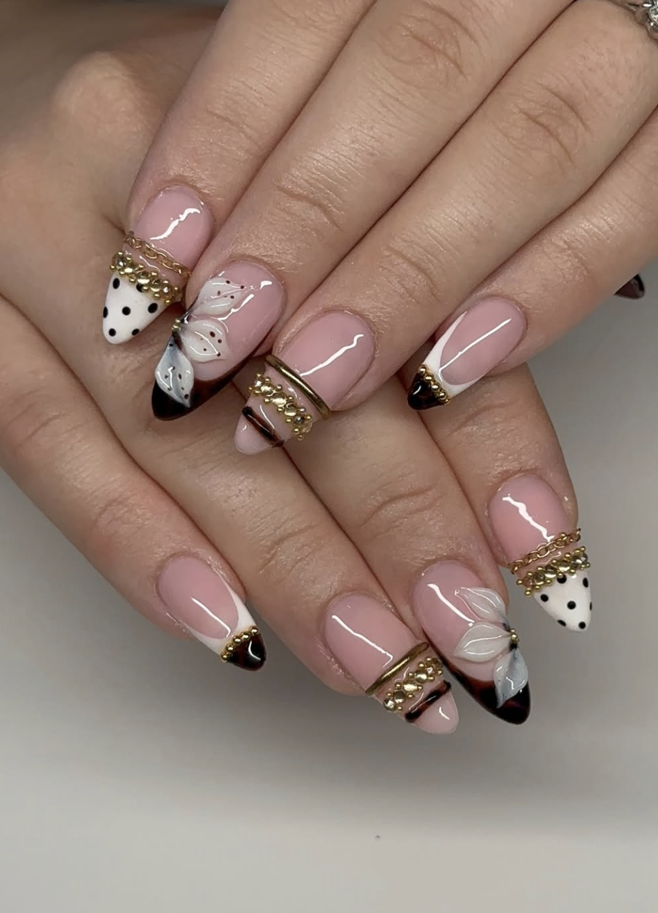 Almond-shaped nails with a mix of white polka dots, French tips, 3D gold chains, and hanging star and pearl charms.