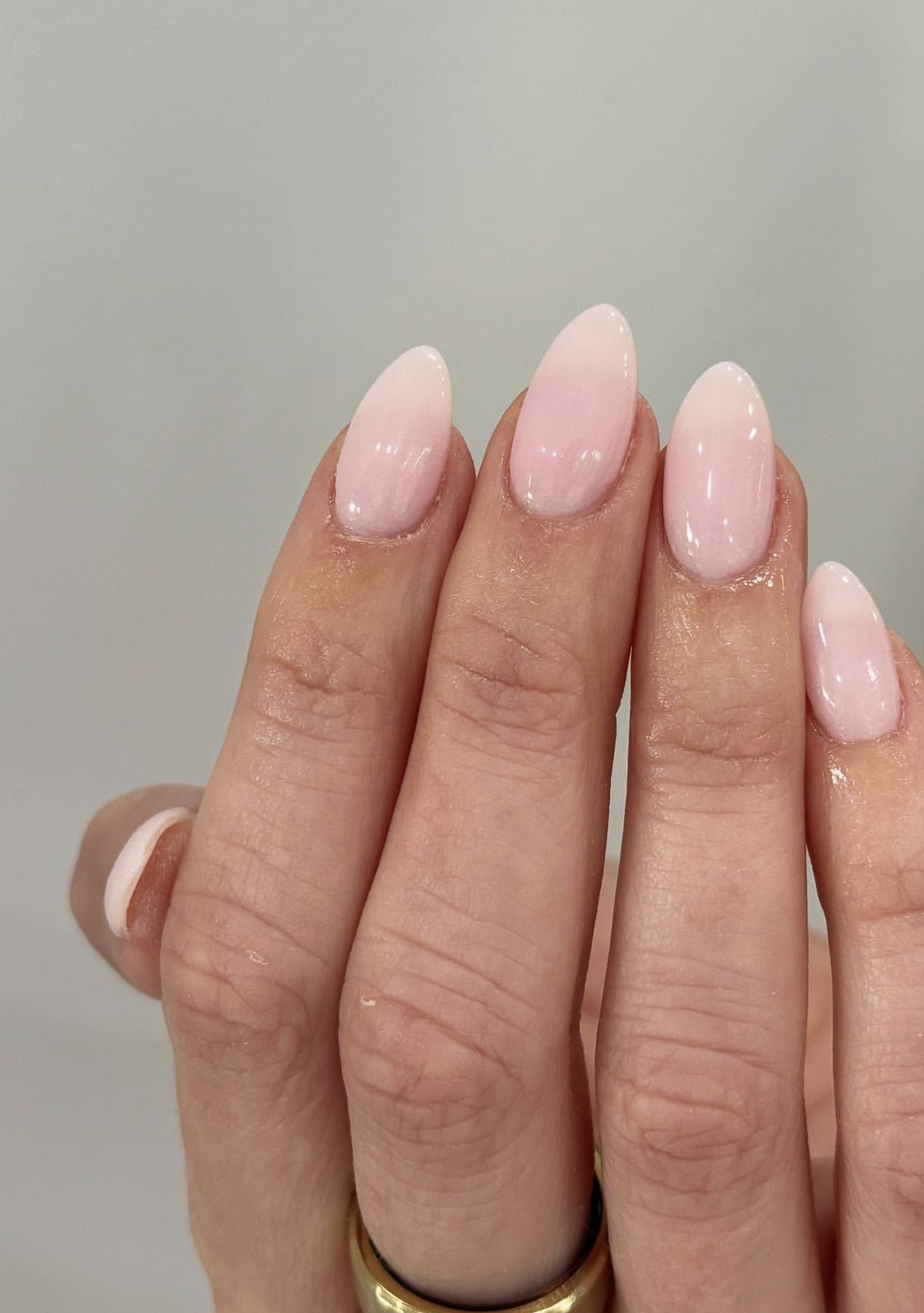 Medium almond nails with a sheer cool-toned pink polish and a high-shine finish.