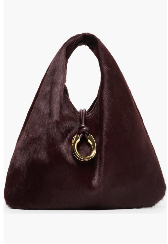 A slouchy deep burgundy calf hair shoulder bag with a gold ring clasp accent and a leather knot detail.