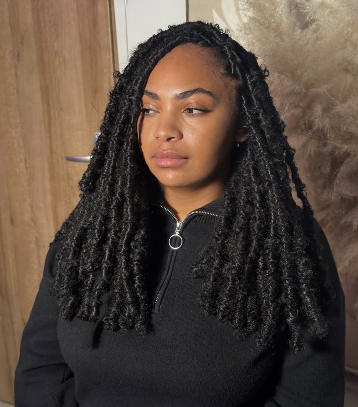 Skai Jackson with mid-length, textured butterfly locs and a middle part, wearing a black zip-up hoodie and showcasing the balanced proportions of a diamond face shape.
