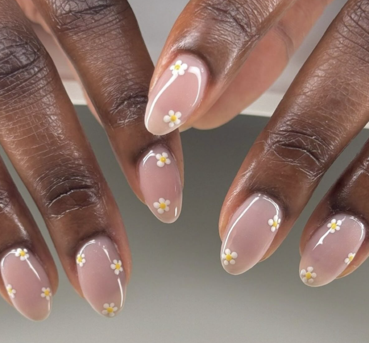 A high-feminine minimalist spring manicure by @__skin. featuring sheer nude almond-shaped nails with delicate, tiny white and yellow hand-painted daisies.