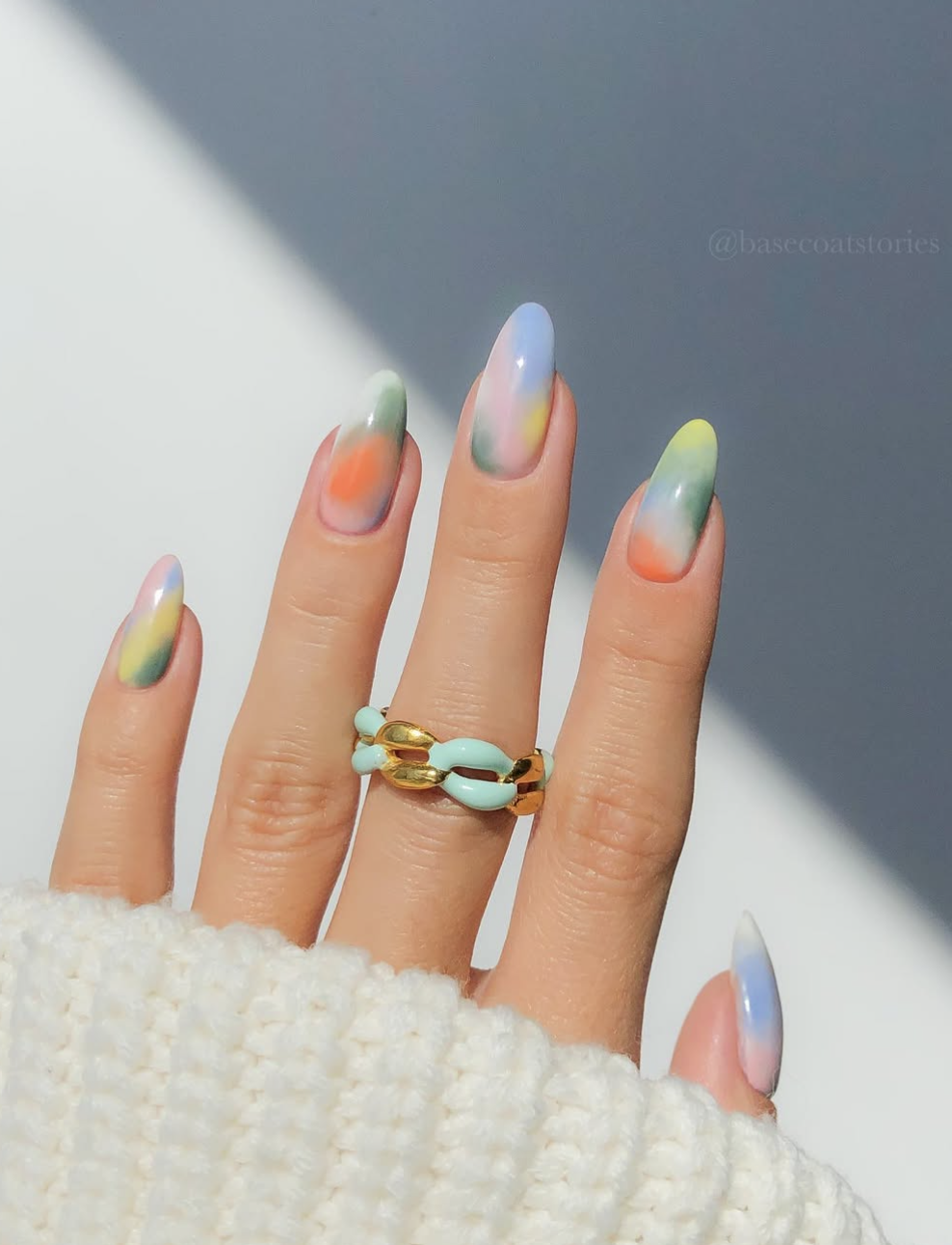Long, oval-shaped nails featuring a soft, airbrushed aura gradient design with bleeding tones of pastel orange, mint green, sky blue, and butter yellow, accented by a chunky mint green chain link ring.