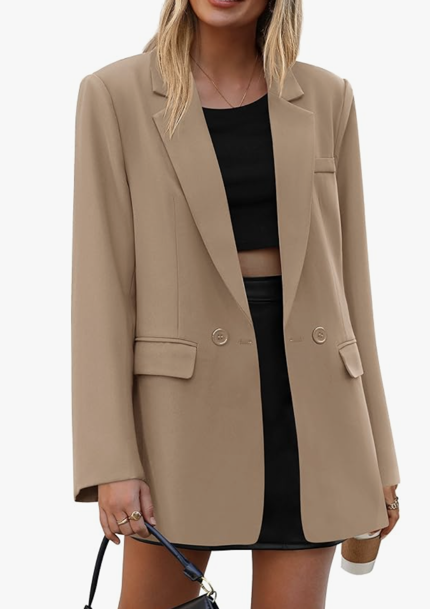 A woman wearing an oversized beige blazer over a black crop top and black leather trousers, demonstrating a modern monochrome outfit formula.