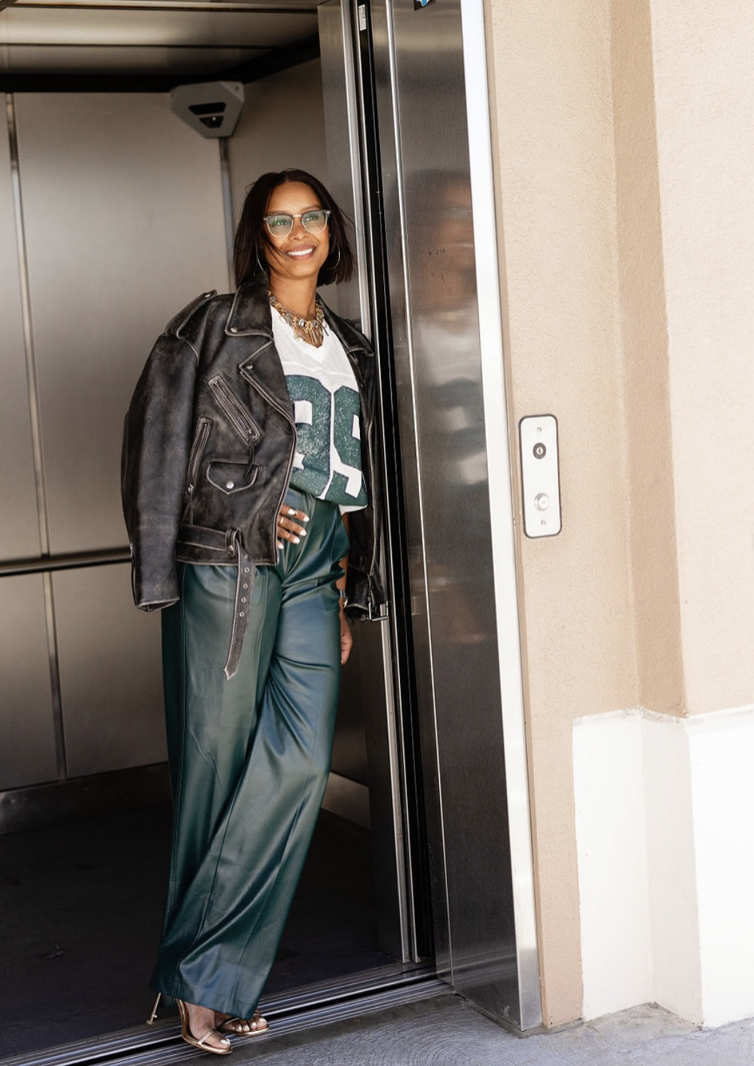 Woman wearing dark green wide-leg leather pants with a black distressed leather moto jacket and jersey t-shirt