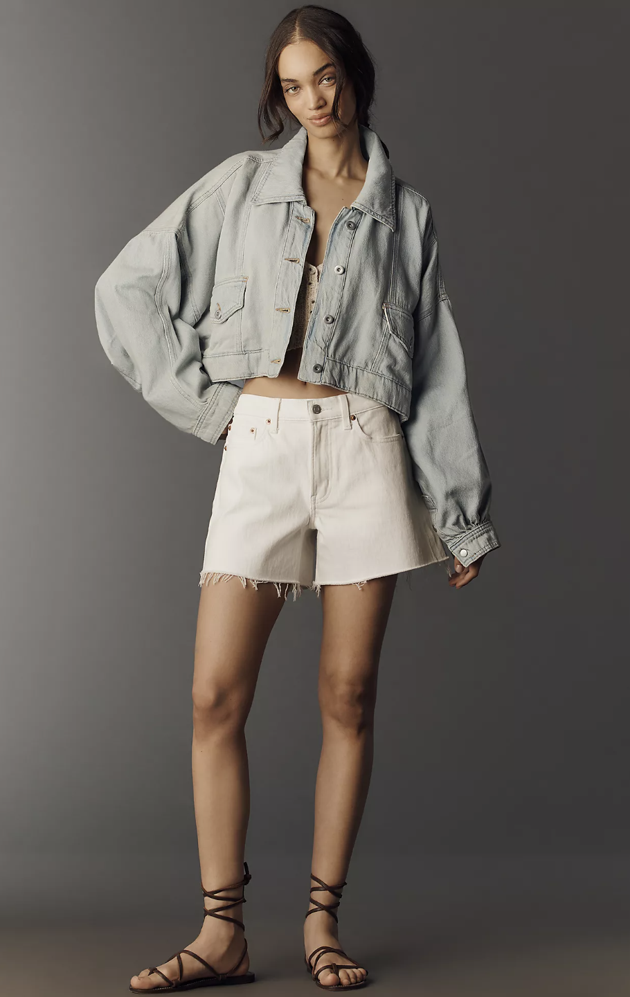 A woman posing in a cropped, light-wash denim jacket paired with high-waisted white denim shorts.