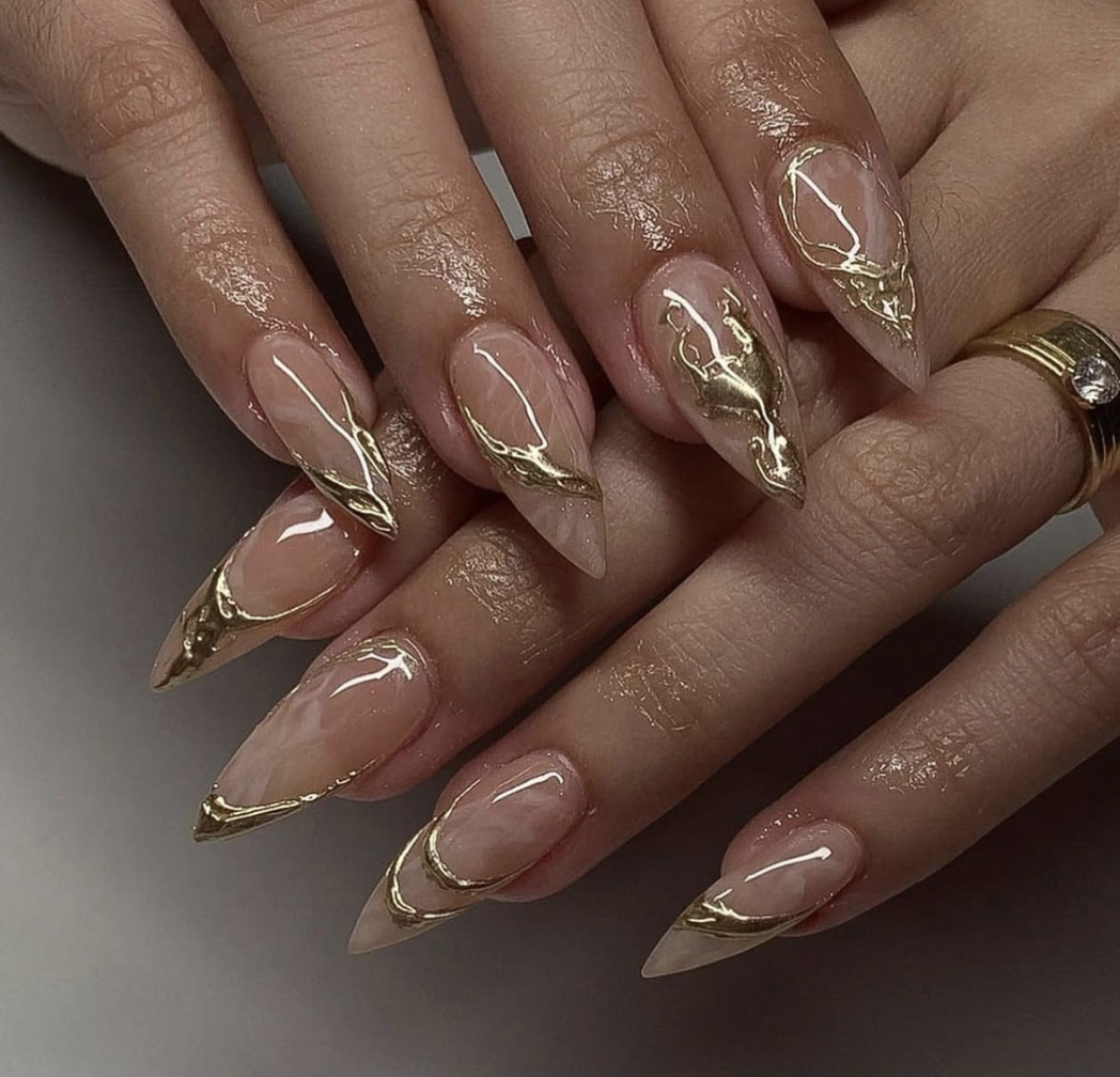 Medium almond-shaped press-on nails with a sheer nude base and 3D metallic gold chrome abstract swirls.