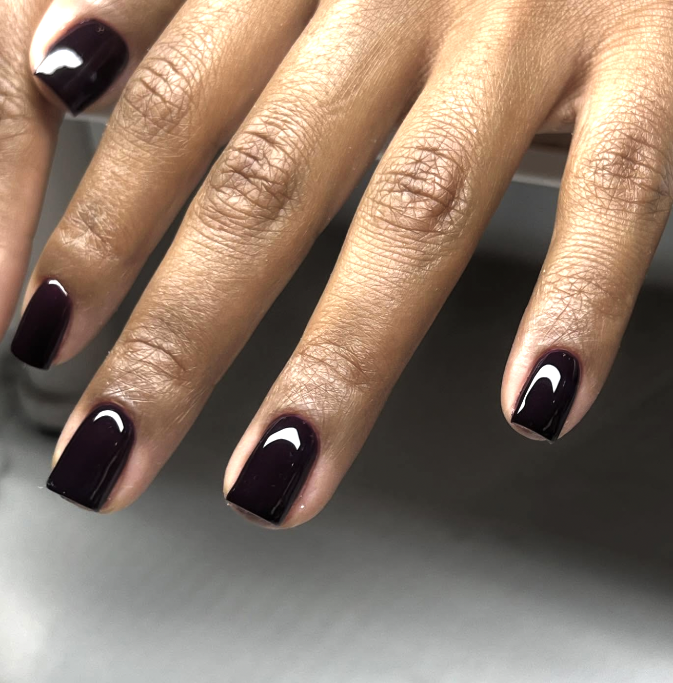 Short round nails painted in a deep glossy oxblood shade.