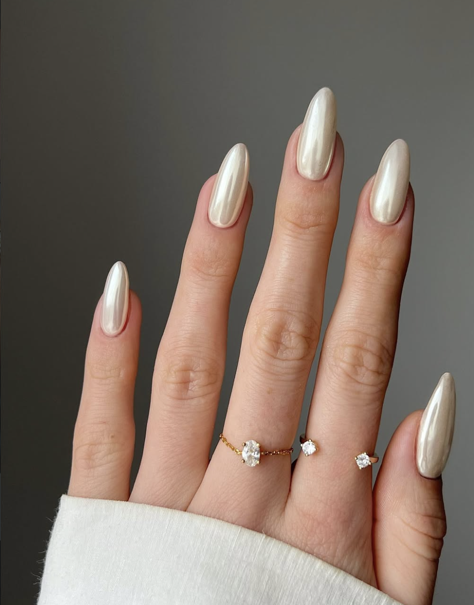 Long, almond-shaped nails featuring a warm beige base coat with a high-shine, luminous pearl chrome glaze finish.