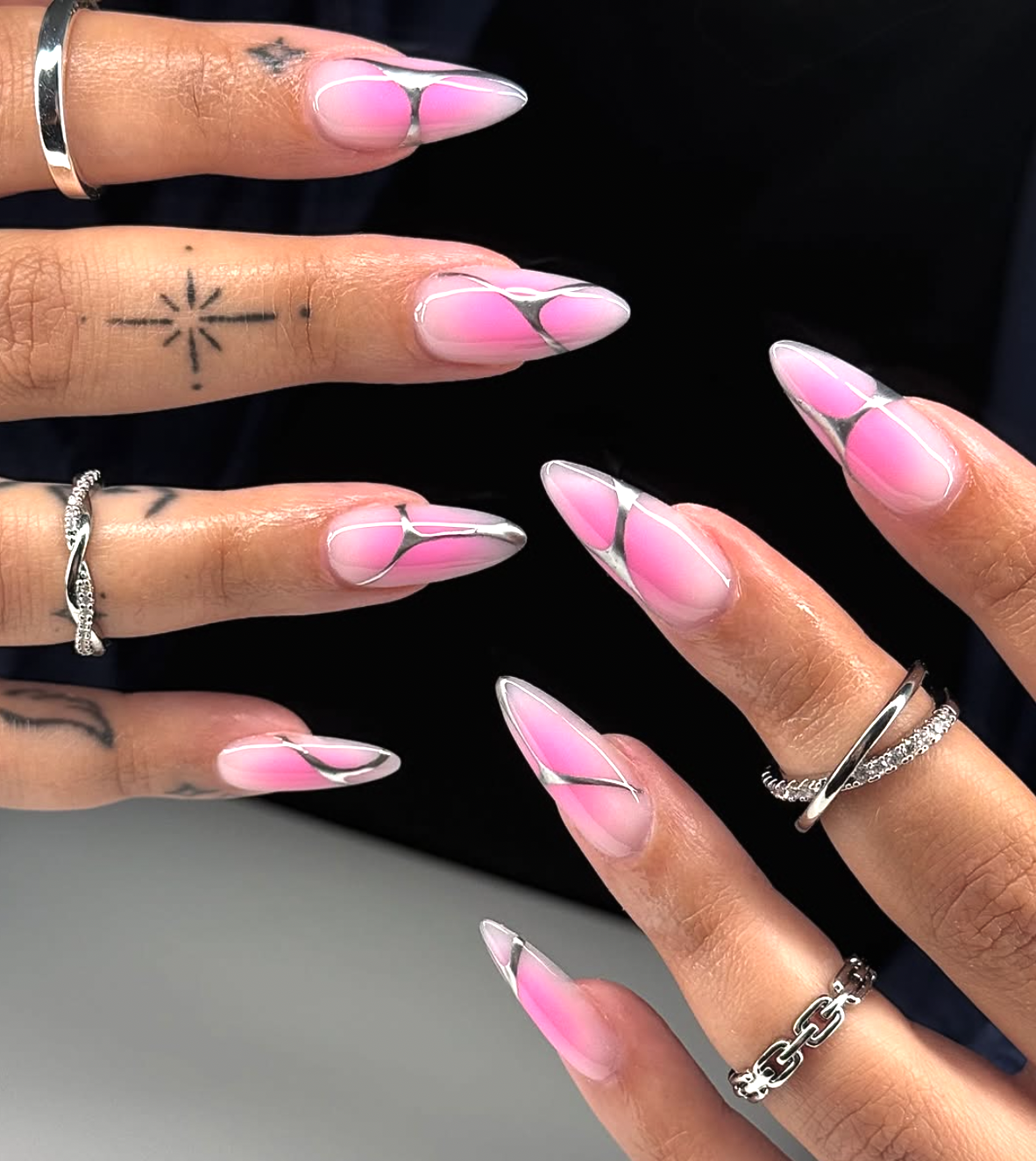 A close-up of long, tapered nails with abstract pink shapes and 3D silver chrome outlines on a sheer base.
