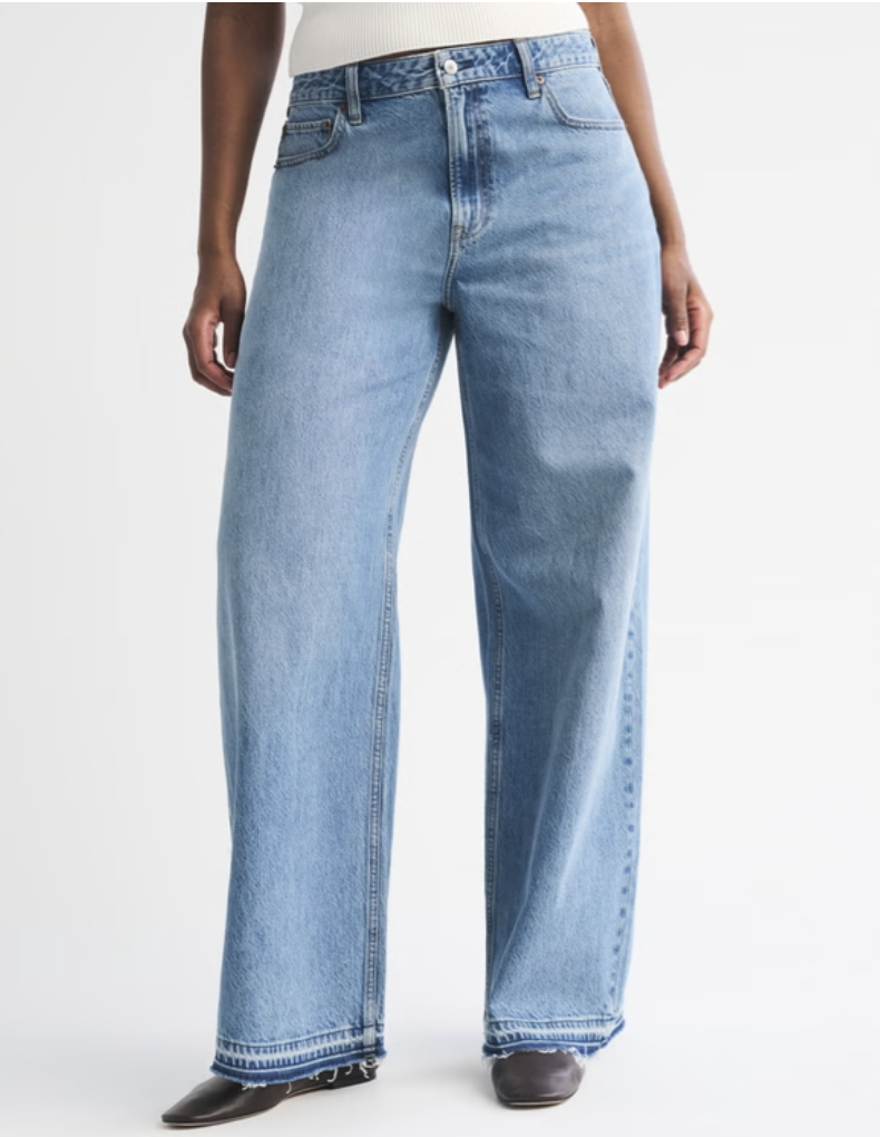 A person wearing light-blue Abercrombie Curve Love High Rise Wide Leg Jeans, showing the extra room through the hip and a clean hem, styled with dark pointed-toe boots.