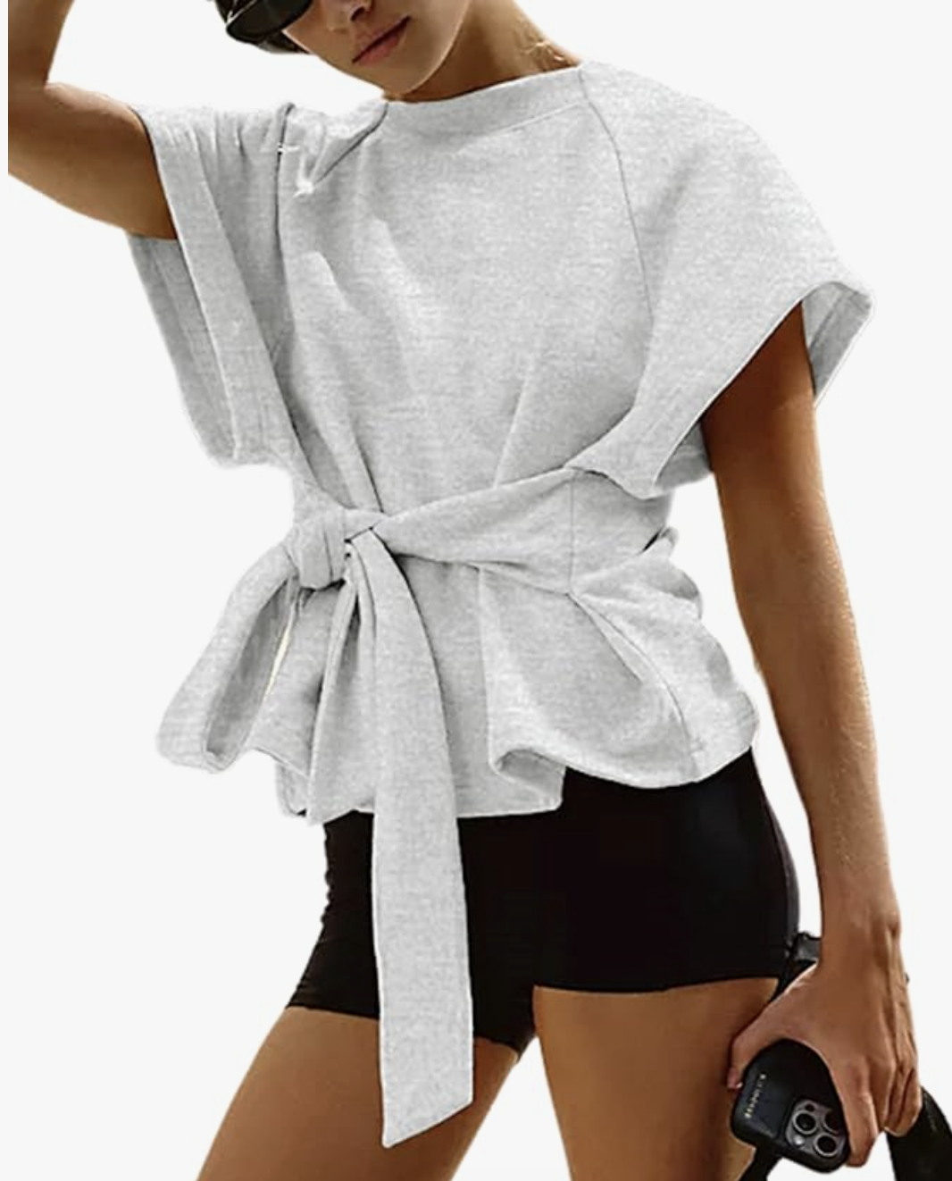 A woman wearing a grey short-sleeve wrap top with a cinched tie waist, styled with black shorts for a casual everyday look.