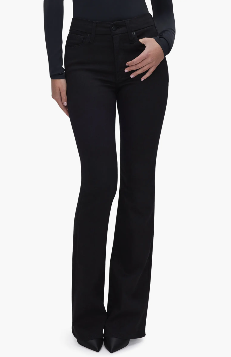 Full-length view of a woman wearing black Good American slim bootcut jeans with a high-rise waist and pointed-toe heels.