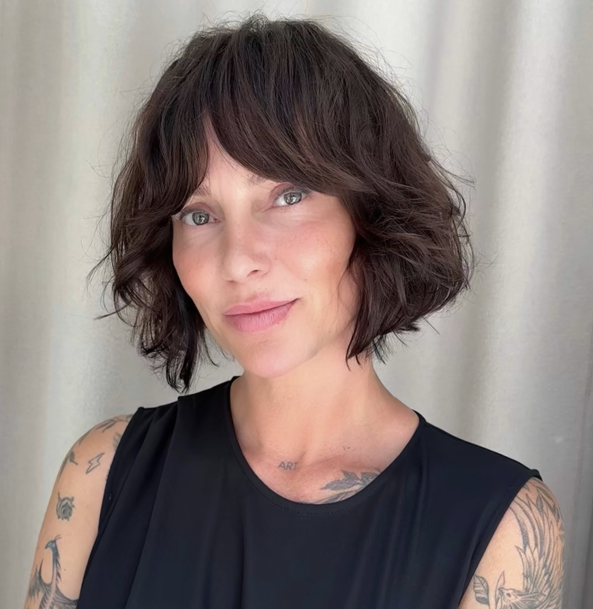 A woman with a modern, textured brunette shaggy bob haircut featuring soft face-framing layers and wispy bangs.