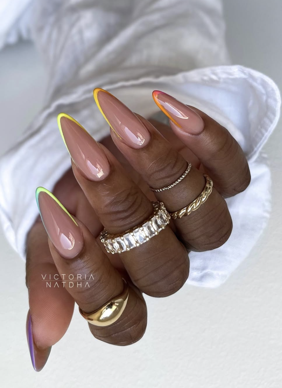 Long almond-shaped gel nails with a sheer nude base and different colored neon and pastel French tips on each finger.