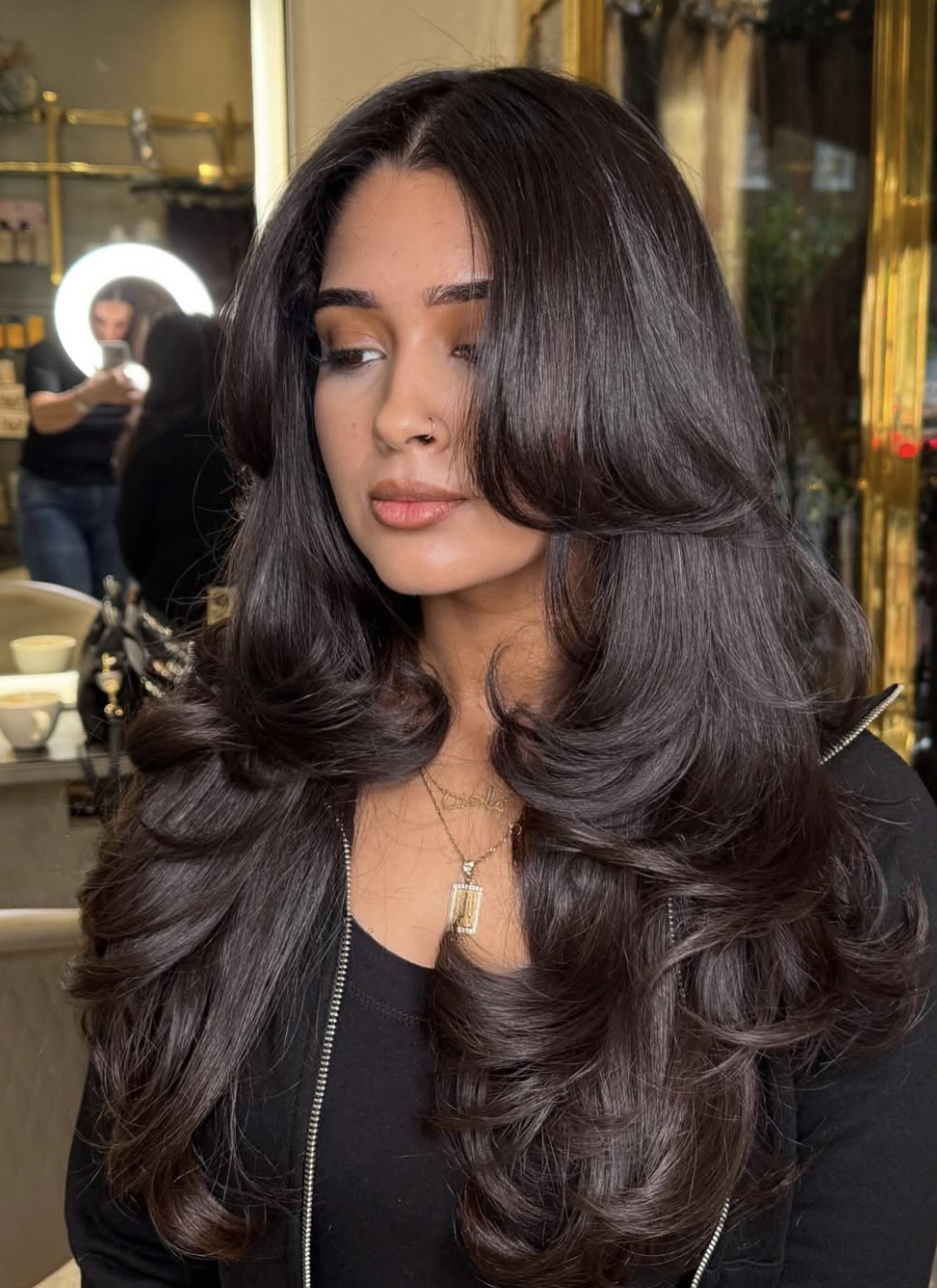 Woman with long, dark, voluminous hair styled in a layered butterfly cut with bouncy curled ends.