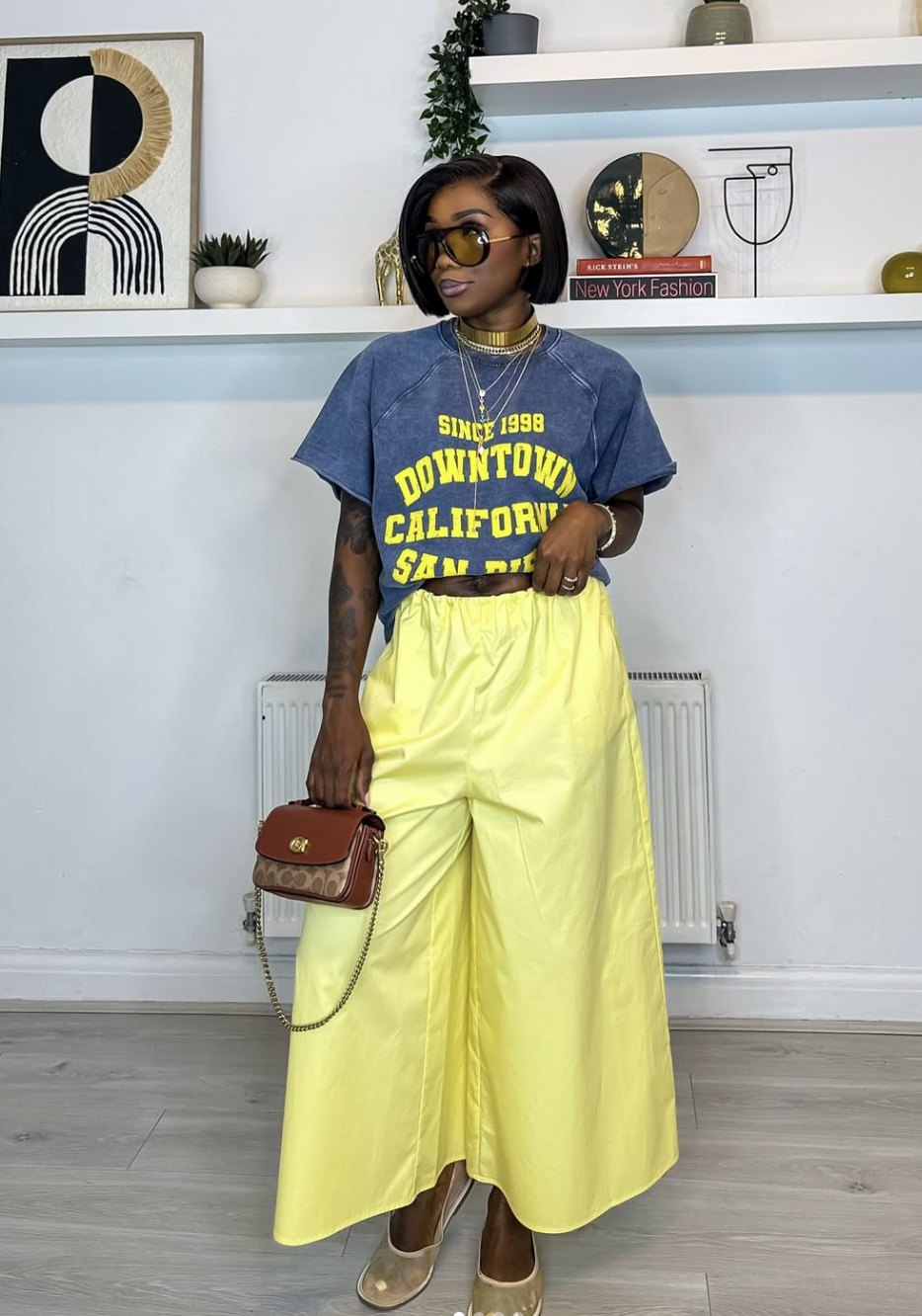 A woman wearing a bright yellow high-waisted maxi skirt with a blue "Downtown California" graphic t-shirt and yellow-tinted sunglasses.