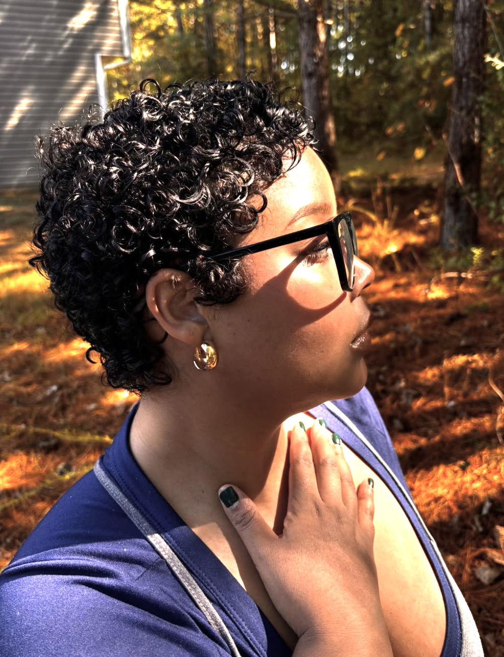 A side profile of Tiana Mone with a short, curly natural pixie cut, wearing gold hoop earrings and glasses while showcasing her sharp diamond face shape bone structure.