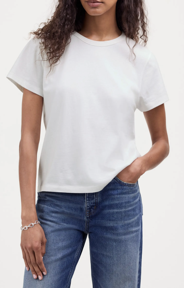 Woman wearing a classic white crewneck t-shirt tucked into blue jeans, featuring a silver chain link bracelet.