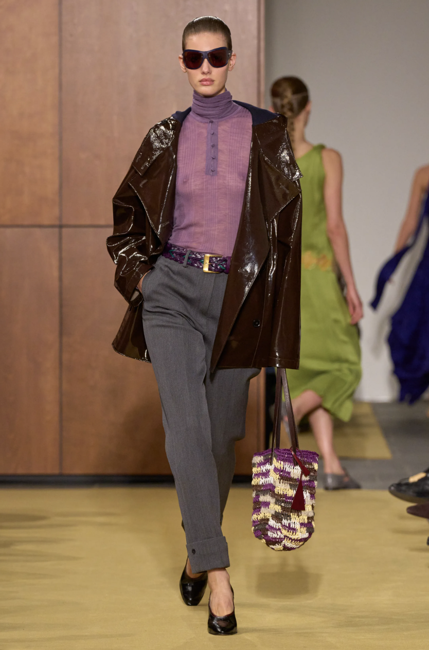 A model on the Tory Burch Fall/Winter 2026 runway wearing a high-gloss aubergine jacket, demonstrating the deep purple power neutral color trend.