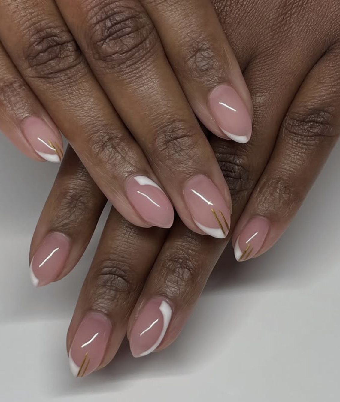 Medium almond-shaped nails featuring a clean white French manicure base with minimalist diagonal gold metallic line accents.