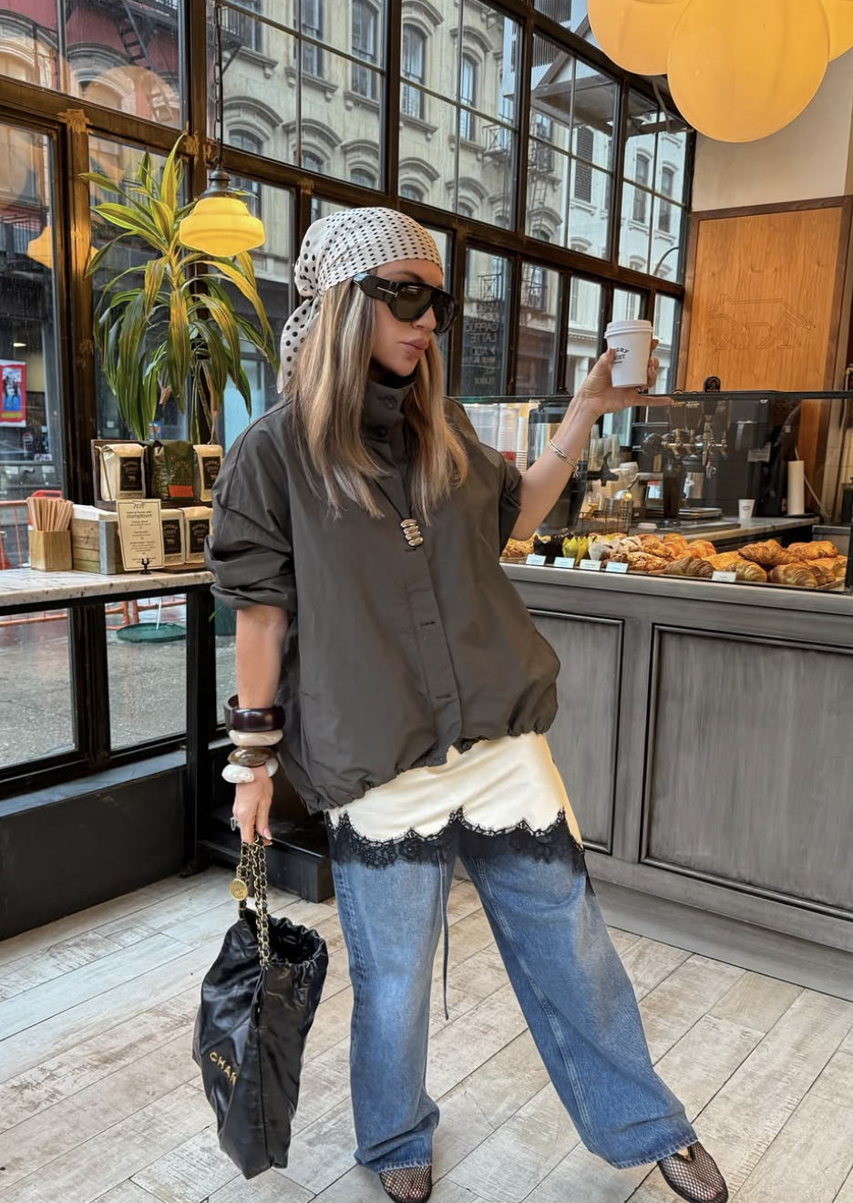 A woman wearing a dark grey oversized button-down over a black satin camisole with prominent black lace trim, paired with blue jeans and a black Chanel 22 bag.