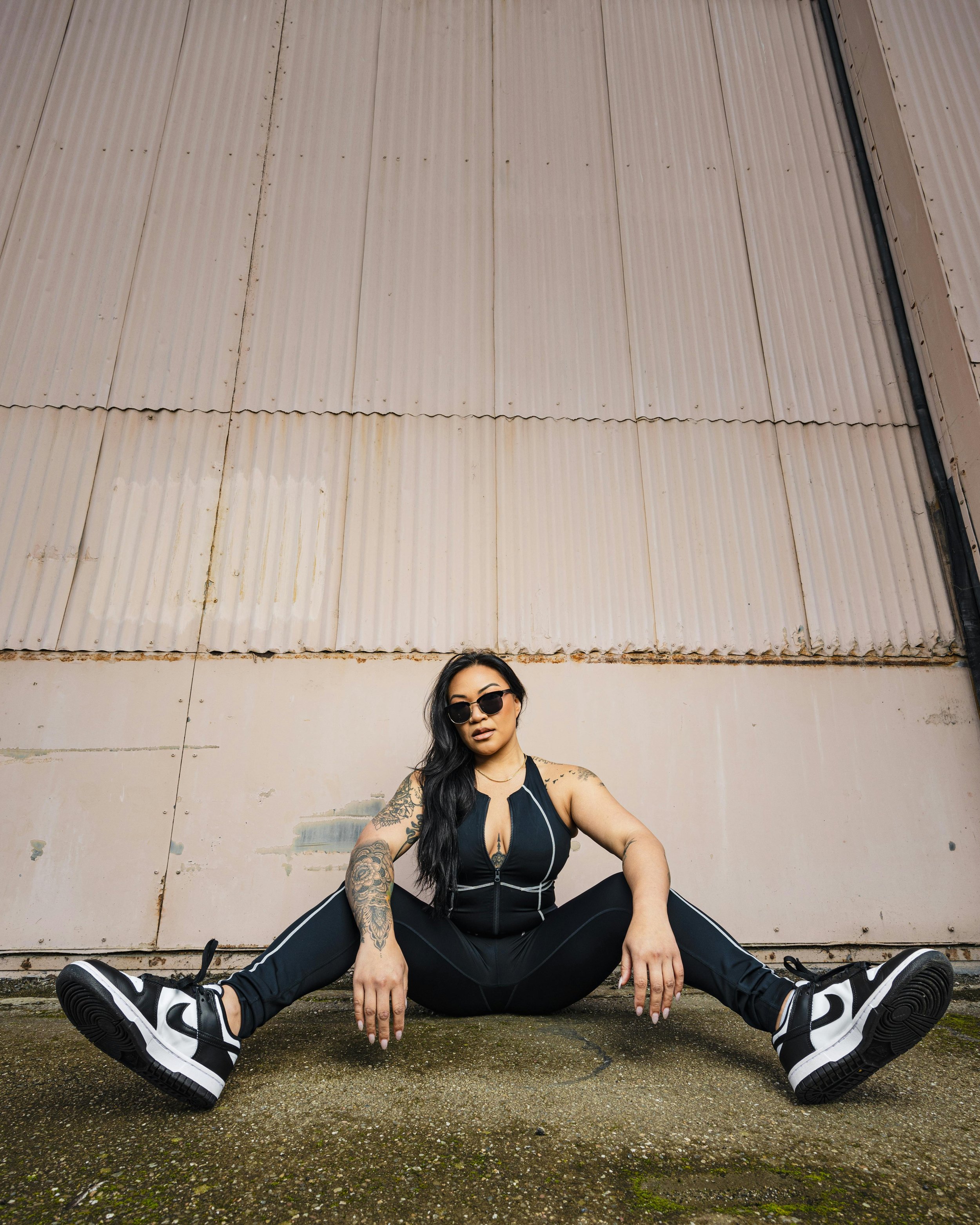 Woman in Sunglasses and with Tattoos Sititng by White Wall
