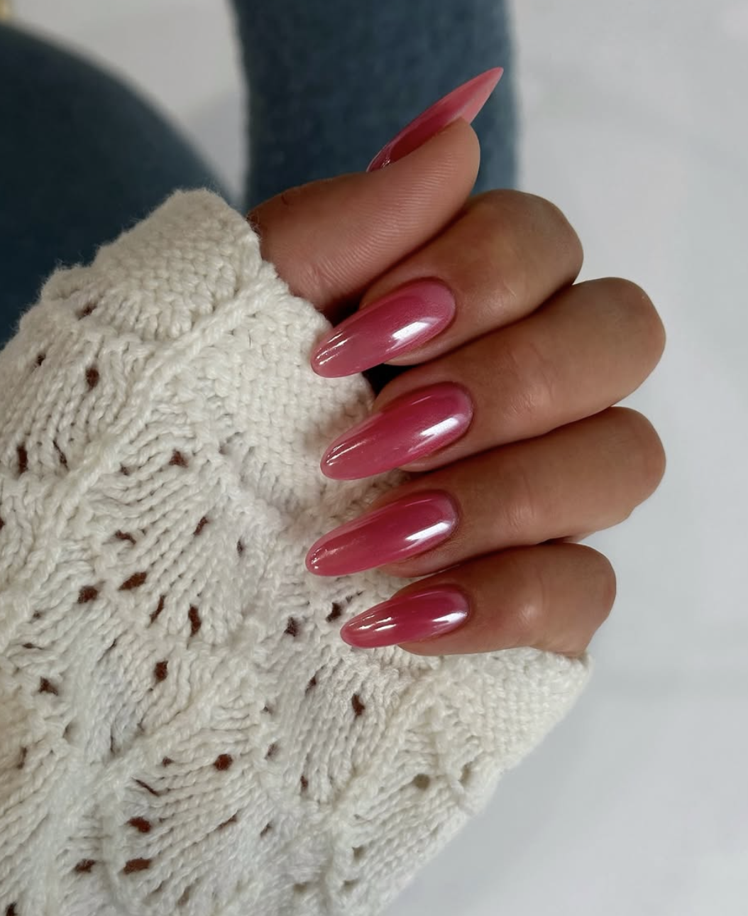 Long almond-shaped nails with a translucent strawberry pink polish and a high-shine iridescent glazed finish.