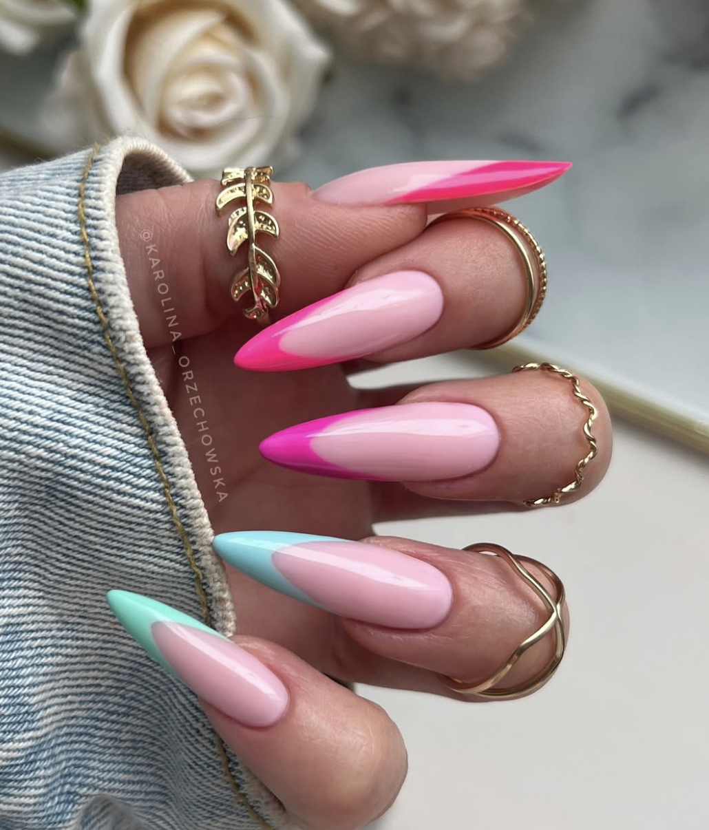 Long stiletto-shaped nails with a smooth pale pink base, featuring vibrant mismatched French tips in hot pink, bright turquoise, and mint green, highlighting cute June nail ideas.
