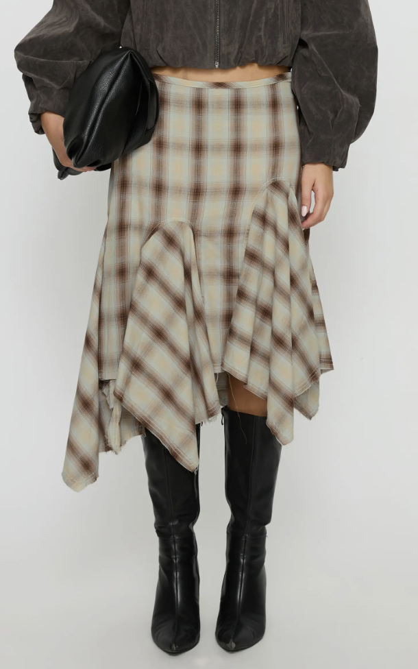 Model wearing a brown and beige plaid skirt paired with black leather knee-high boots on a white background.