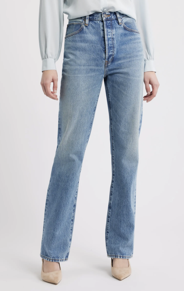 A woman wearing light-wash, high-waisted relaxed straight-leg jeans by FRAME, paired with a light blue long-sleeve blouse and tan pointed-toe heels.