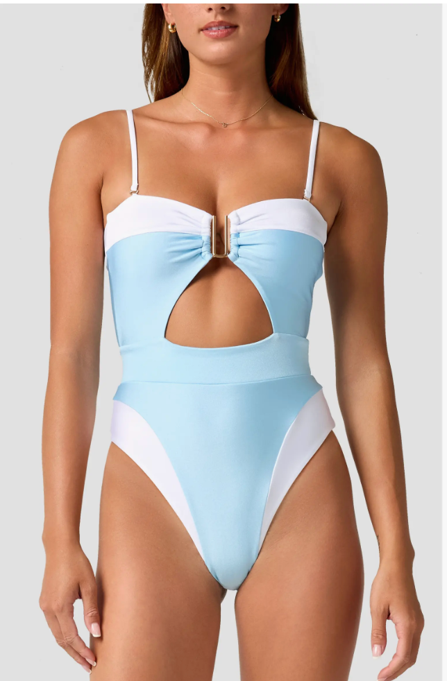 A woman wearing a light blue and white color-blocked one-piece swimsuit with a front cutout and strappy details, styled as a versatile option for vacation packing.