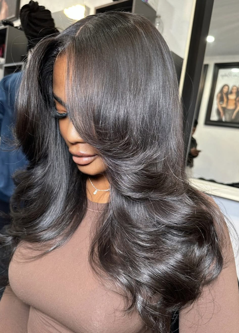 A woman with dark hair and a bouncy butterfly haircut featuring feathered, face-framing layers and soft curls.